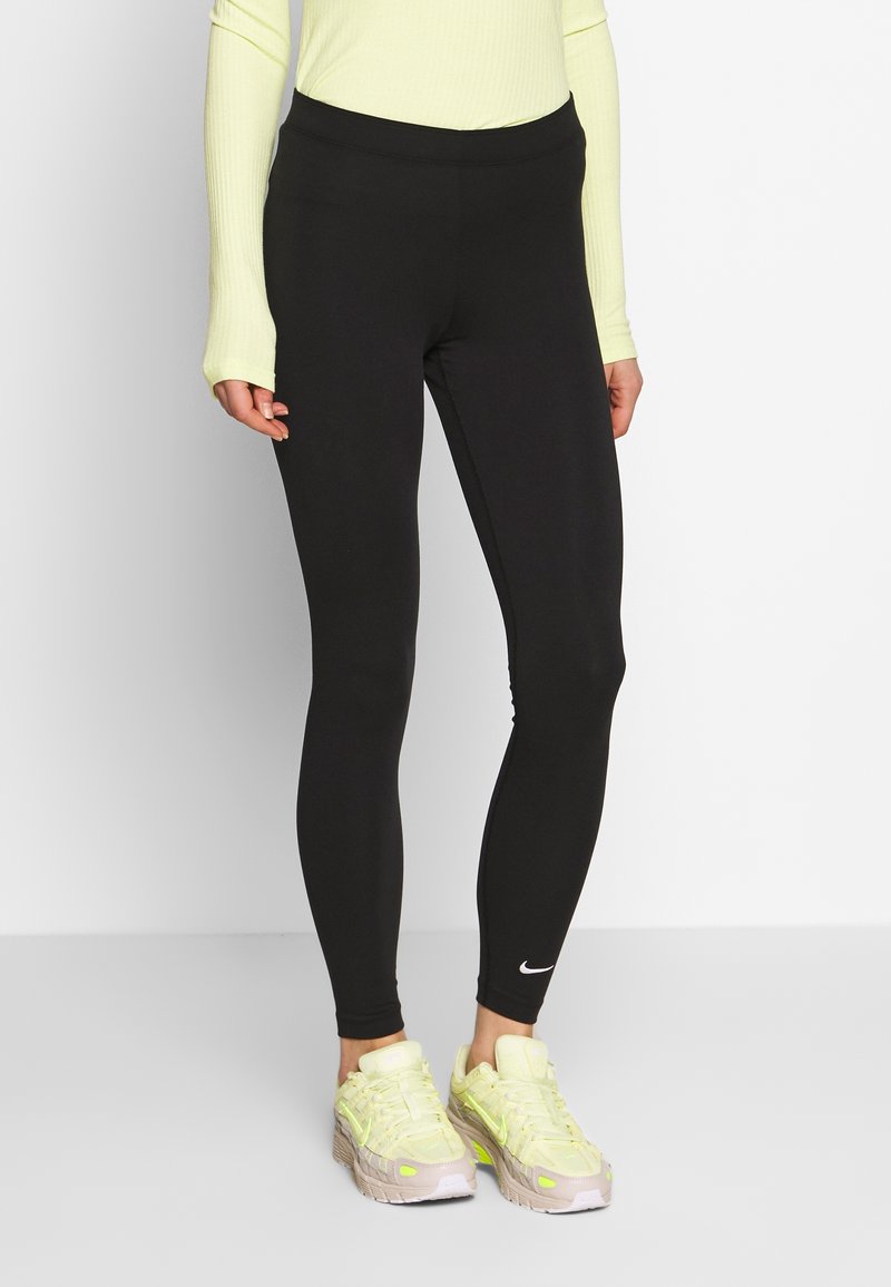 Svarta leggings med hög midja, tillverkade av stretchmaterial. Har en liten vit Nike-logotyp vid fållen. Kombineras med ljusa träningsskor.