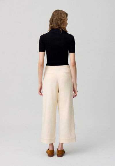Haut noir à rayures à manches courtes associé à un pantalon large crème. Les détails notables incluent le col et les coutures de la poche arrière.