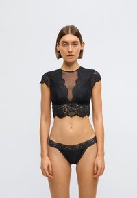 Čierna čipkovaná súprava spodnej bielizne s krátkym topom s krátkymi rukávmi a podpásaným lemom, doplnená zodpovedajúcimi nízko posadenými nohavičkami.