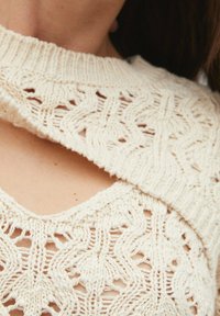 Crème gebreide trui met een ingewikkeld open patroon en een brede halslijn, die een delicate textuur en zachte garen laat zien.