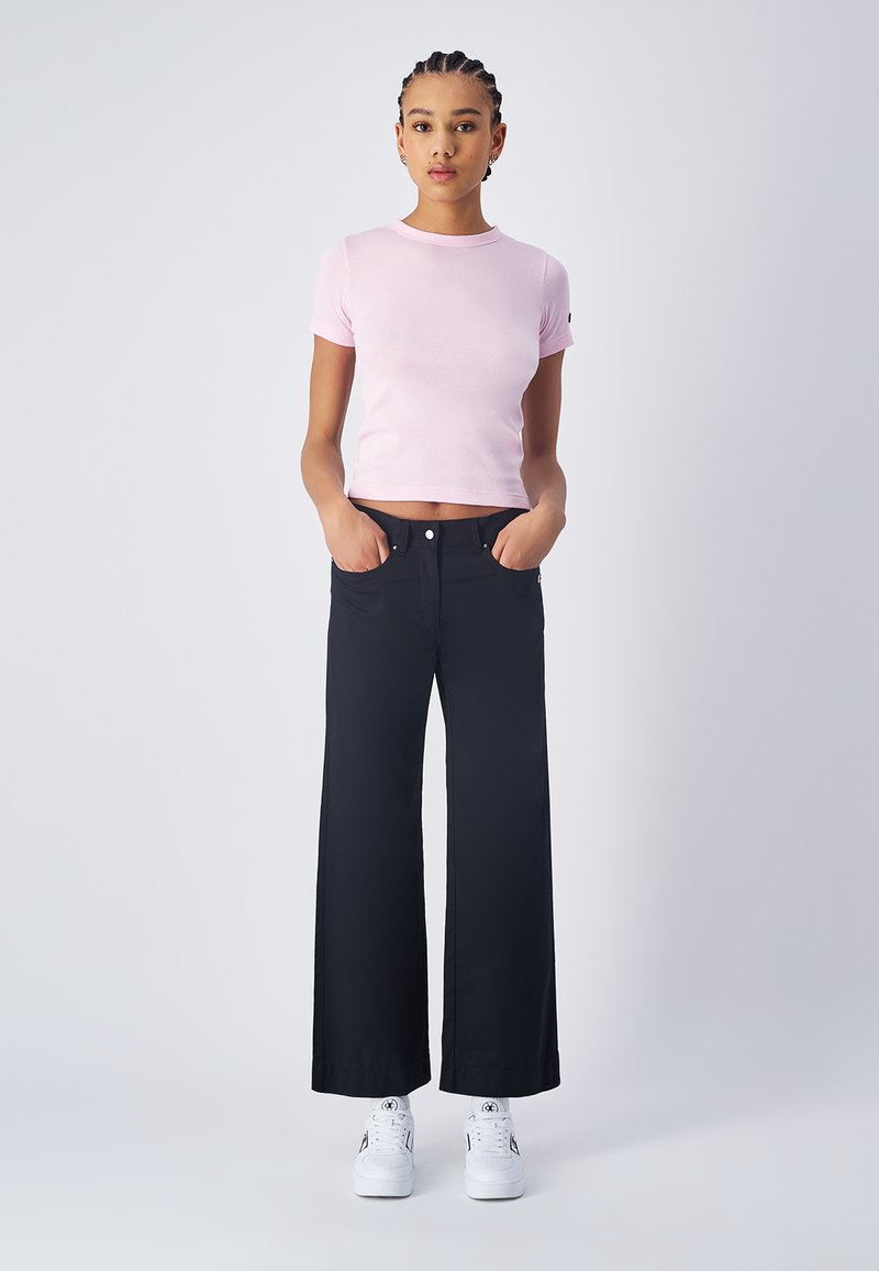 Top rosa a maniche corte abbinato a pantaloni neri a gamba larga e sneakers bianche. Il top è aderente; i pantaloni hanno un'alta vita e una texture in denim.