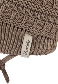 Brown knitted hat with a textured design. Features a branded fabric tag. Ties at the chin for secure wear.