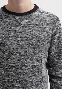 Felpa a maglia marled nera e grigia con scollatura rotonda, colletto a coste e tessuto testurizzato. Maniche lunghe che arrivano ai polsi.