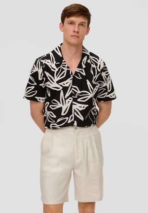Chemise noire à manches courtes avec un motif de feuilles blanches, associée à un short crème taille haute ; les deux sont fabriqués en tissu léger.