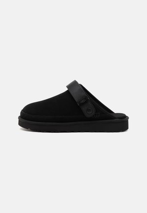 Pantof cu slip-on din suede negru, cu o curea lata care are o clapeta circulara. Talpa groasa din cauciuc negru si textura neteda. Design minimalist.