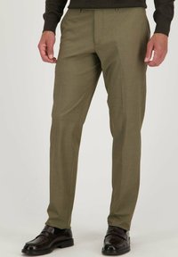 Pantalons verts olive en tissu lisse avec une coupe ajustée, dotés d'un devant plat et de poches latérales, associés à des chaussures en cuir marron foncé.