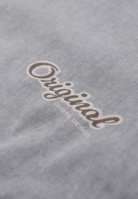 Tela gris con una textura suave que presenta un logotipo en cursiva "Original" en rosa claro y "OMBRÉ DESIGN" en texto más pequeño.