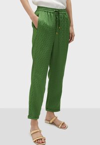 Green patterned trousers with an elastic waistband and drawstring. They feature side pockets and a tapered leg design.