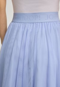 Ljust blå tyllkjol med bred midja prydd med upprepade "JOOP!"-logotyper, bärs med en vit topp.