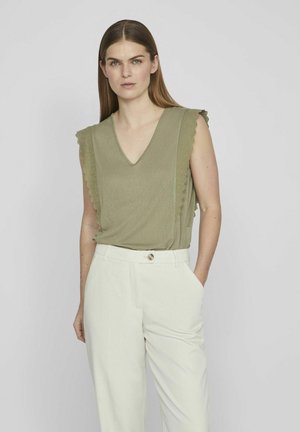 Top sin mangas de color verde oliva con un escote en V y bordes de mangas con puntilla, combinado con pantalones de cintura alta en color crema. Textura de tela suave.