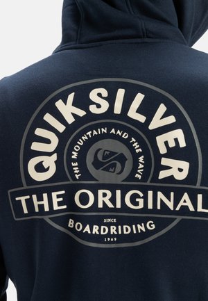 Navy blue hoodie with a large circular graphic on the back, featuring white text "QUIKSILVER" and "THE ORIGINAL" along with brand imagery.