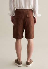 Pantaloni corti in lino marrone con vita elastica e due tasche posteriori. I pantaloni corti hanno una vestibilità comoda e arrivano sopra il ginocchio.