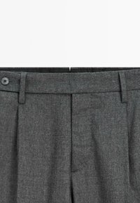 Pantaloni in misto lana grigi con frontale piatto, chiusura a bottone singolo e passanti per cintura. Presentano una texture sottile e un design su misura.