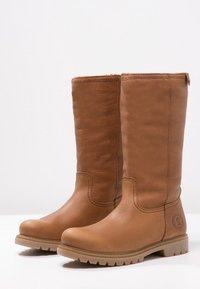 Stivali in pelle marrone al ginocchio con suola piatta, dettagli cuciti e punta rotonda. Presenta un logo sul lato esterno.