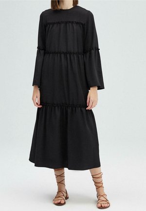 Robe midi noire à manches longues, avec des volants froncés à la taille et aux manches. Fabriquée dans un tissu doux et fluide.