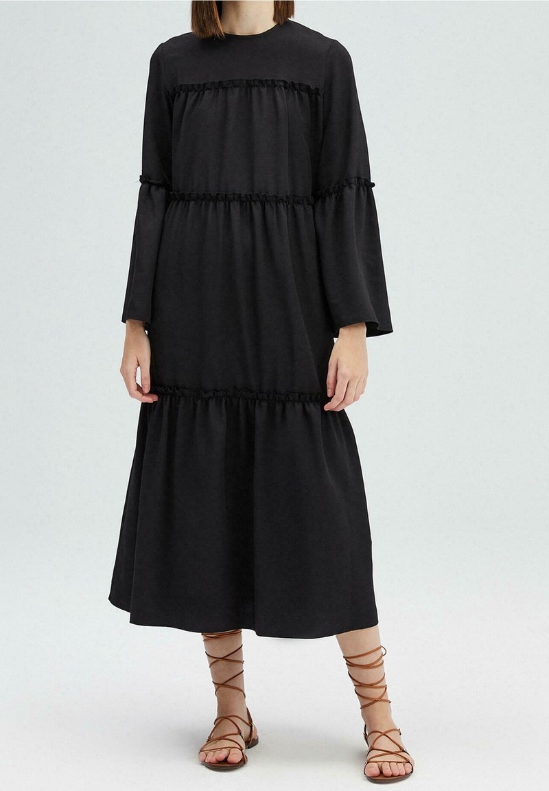 Robe midi noire à manches longues, avec des volants froncés à la taille et aux manches. Fabriquée dans un tissu doux et fluide.