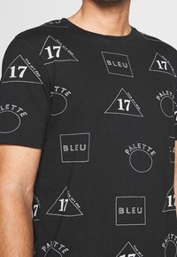 Camiseta de algodón negra con formas geométricas y texto en blanco, que incluye triángulos, círculos y cuadrados con las palabras "BLEU" y "PALETTE."