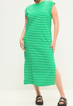 Femme portant une robe midi sans manches à rayures horizontales vertes et blanches avec une fente sur le côté et des sandales noires à boucle.