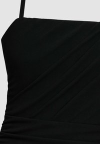 Tessuto nero con pieghe diagonali e una sottile spallina, che forma la parte superiore di un capo aderente.