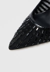 Scarpa nera con punta a punta, tomaia in tessuto strutturato con strisce verticali e piccoli accenti rettangolari. Interno in morbida pelle nera.