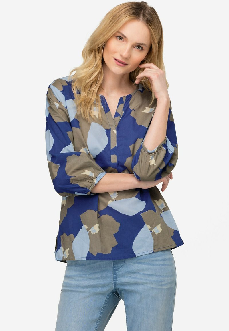Blusa floreale blu e beige con scollatura a V, maniche a tre quarti e polsini arricciati. Tessuto liscio, vestibilità comoda, materiale leggero.