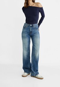 Navy off-shoulder long-sleeve top paired with light blue wide-leg jeans. Jeans feature a high waist, five pockets, and subtle fading.