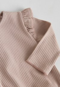 Hladký jemne ružový textil s ryhami, ktorý má volánový golier a lemovanie rukávov, s jemným prešívaním a hladkým povrchom.