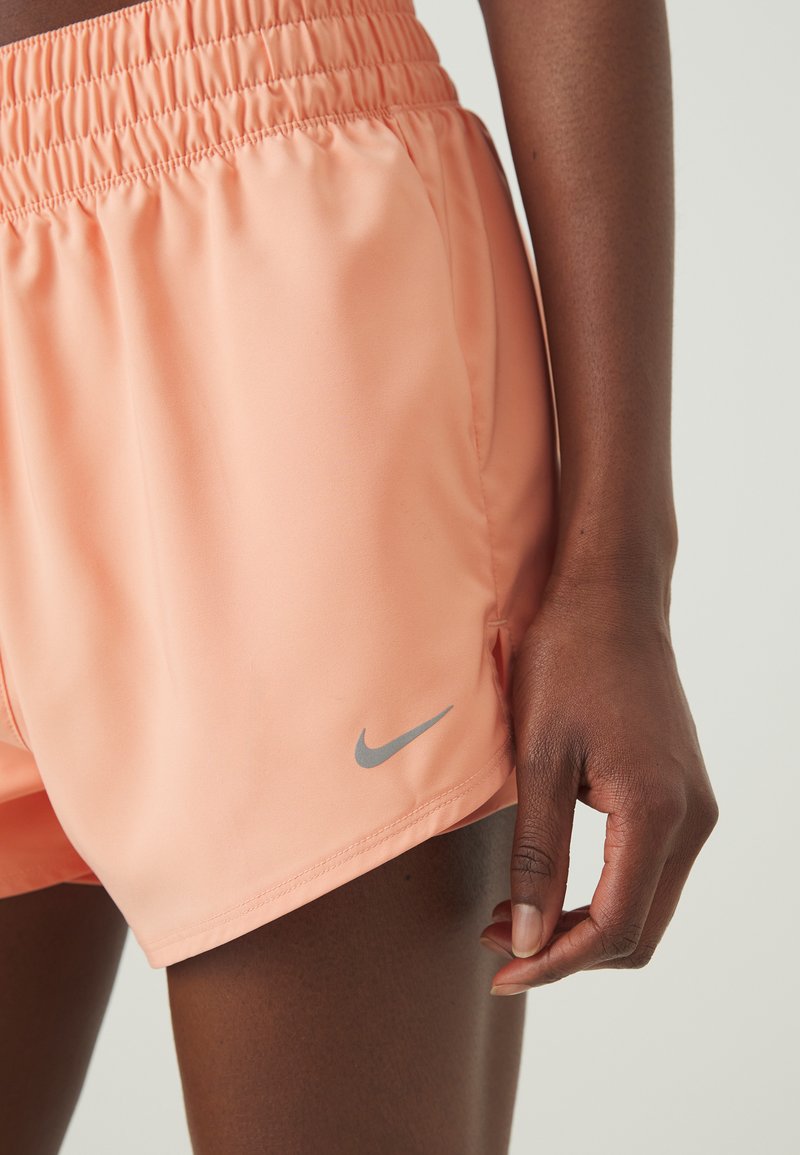 Shorts Nike couleur pêche avec une taille élastique et un logo gris, en tissu léger et dotés de poches latérales. Texture lisse.