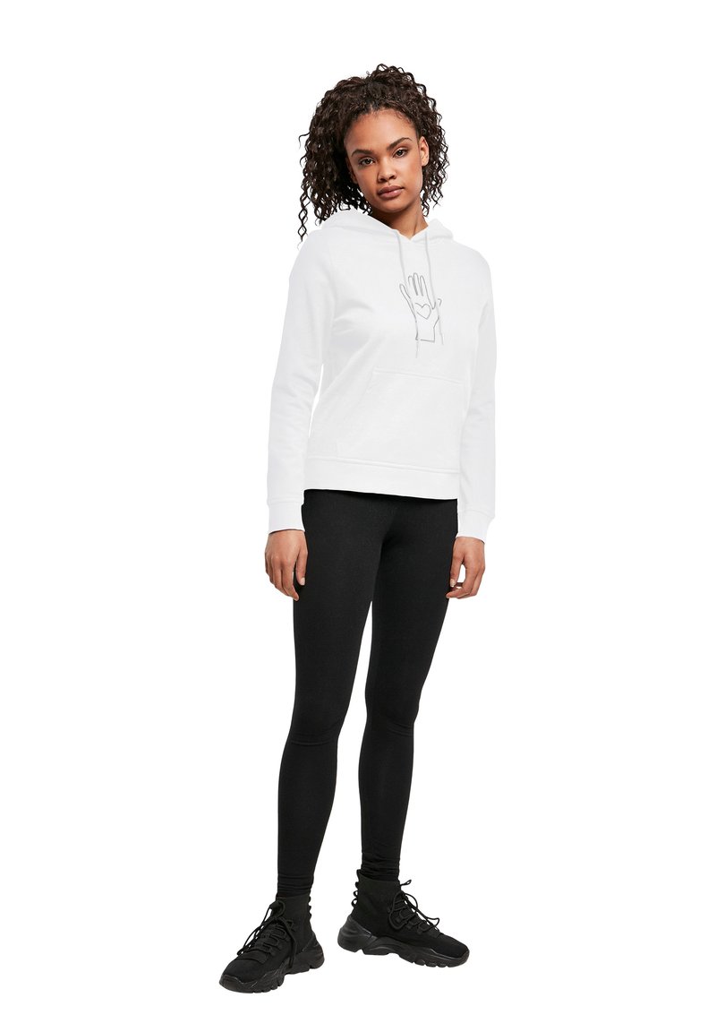 Vit huvtröja med en handgrafik, framficka i kängurustil, bärs med svarta leggings och svarta träningssneakers.