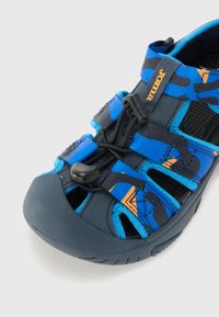 Blå och mörkgrå sportsandaler med justerbara remmar, en texturerad gummisula och ett dragkedjesystem för säker passform.