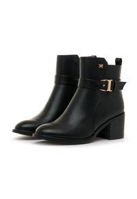 Botas de tobillo negras hechas de cuero suave con un panel lateral texturizado, una correa con hebilla y un tacón cuadrado. Detalles decorativos en dorado.