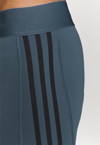 Niebieskie legginsy z elastycznej tkaniny z szerokim pasem i trzema czarnymi pionowymi paskami po bokach. G�ładka tekstura i dopasowany krój.