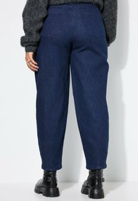 Dunkelblaue Denim-Jeans mit weitem Schnitt, ausgestattet mit zwei Gesäßtaschen und einer hohen Taille. Kombiniert mit schwarzen Stiefeletten und einem strukturierten grauen Pullover.