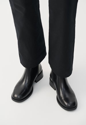 Black leather chelsea boots with a smooth texture, rounded toe, and a low block heel, paired with black pants.