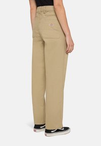 Beige wijde broek met een hoge taille, achterzakken en een gestikte logo. Gecombineerd met zwarte sneakers met witte accenten.