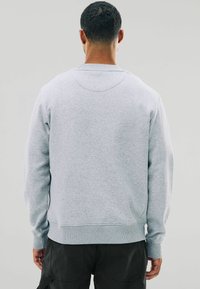 Sudadera gris hecha de una tela suave, con cuello redondo, mangas largas y puños de canalé, con un diseño sencillo y sin patrones visibles.