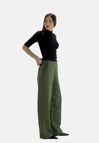 Zwart nauwsluitend bovenstuk met korte mouwen, gecombineerd met wijduitlopende, hoge taille olijfgroene broek met steekzakken aan de voorkant. Glad stoffen oppervlak.