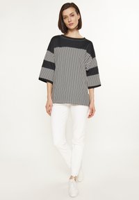Schwarz-weiße gestreifte oversized Bluse mit kurzen Ärmeln, kombiniert mit weißen Hosen und weißen Sneakern. Glattes Material, lässige Passform.