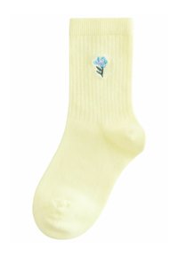 Chaussettes jaunes à côtes avec une petite broderie de fleur bleue sur le côté. Texture douce avec un design standard à la cheville.