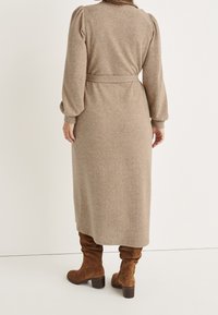 Lång, ljusbrun stickad klänning med ribbad struktur, midja med bälte och puffärmar, kombinerad med bruna knähöga stövlar i mocka.