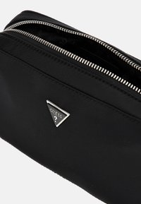 Black nylon pouch with silver zipper, featuring a triangular metal logo detail. Smooth texture with a simple design and interior lining.