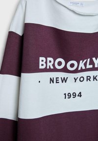 Bordový a svetlomodrý sveter s horizontálnymi pruhmi a výrazným bielym textom "BROOKLYN NEW YORK 1994" na prednej strane. Mäkčená textúra.