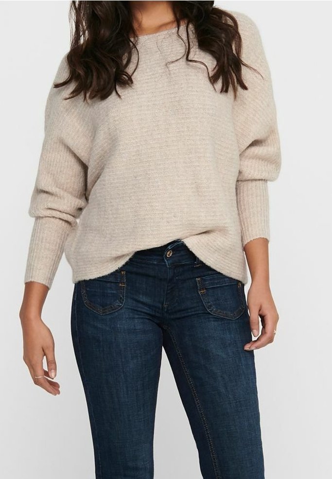 Pull beige côtelé avec épaules tombantes associé à un jean en denim bleu foncé avec coutures claires et design classique à cinq poches.