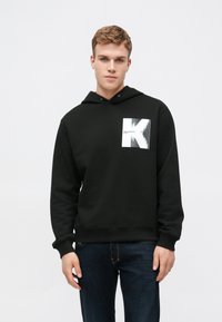 Felpa nera con tasca frontale, caratterizzata da un design grafico bianco e un logo. Tessuto morbido, vestibilità casual e cappuccio regolabile con coulisse.