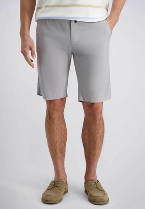 Homme portant un short gris clair jusqu'aux genoux, des chaussures décontractées beiges, et une chemise légère rayée avec les mains dans les poches.