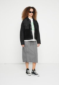 Fekete texturált felületű farmerdzseki, fehér grafikus póló, szürke cargo szoknya és fekete magas szárú tornacipők. Kiegészítők: napszemüveg.