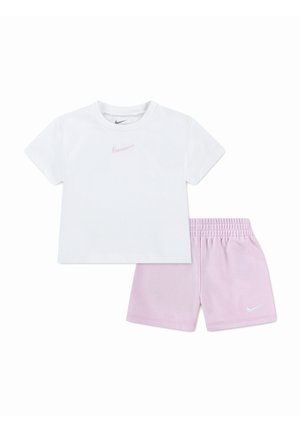 T-shirt bianca a maniche corte Nike con logo swoosh rosa abbinata a pantaloncini Nike rosa chiaro con vita elastica e logo swoosh bianco.