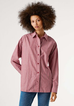 Camisa de rayas rojas y blancas con mangas largas, con botones en la parte delantera y un corte holgado. Tejido suave con cuello clásico y botones rojos.