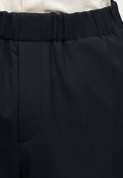 Κοντινό πλάνο μαύρων παντελονιών με ελαστική μέση, εμφανείς άκρες τσέπης και μερικό τμήμα του λευκού τοπ που είναι περασμένο μέσα.