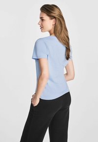 Jasnoniebieska krótkozwałkowa koszulka z okrągłym dekoltem, gładką teksturą i lekko zaokrąglonym dołem, w połączeniu z czarnymi szerokimi spodniami.